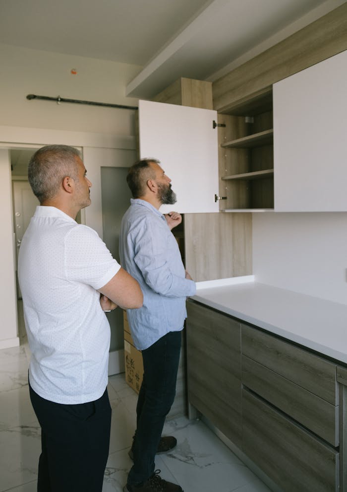 Two men inspecting modern wooden kitchen cabinets in an indoor setting.